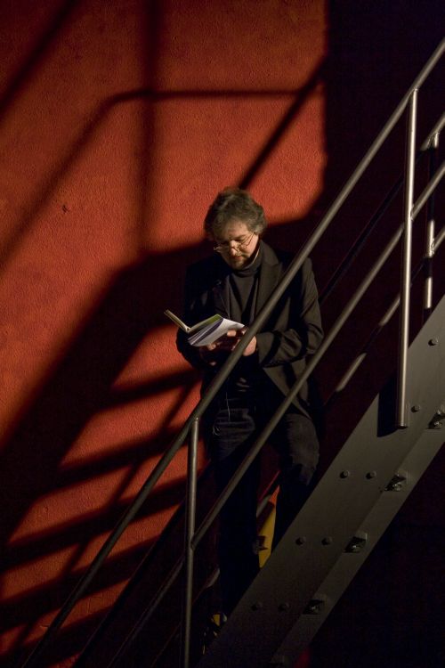 Beat Rink auf einer Treppe vor einem roten Hintergrund in ein Buch blickend.