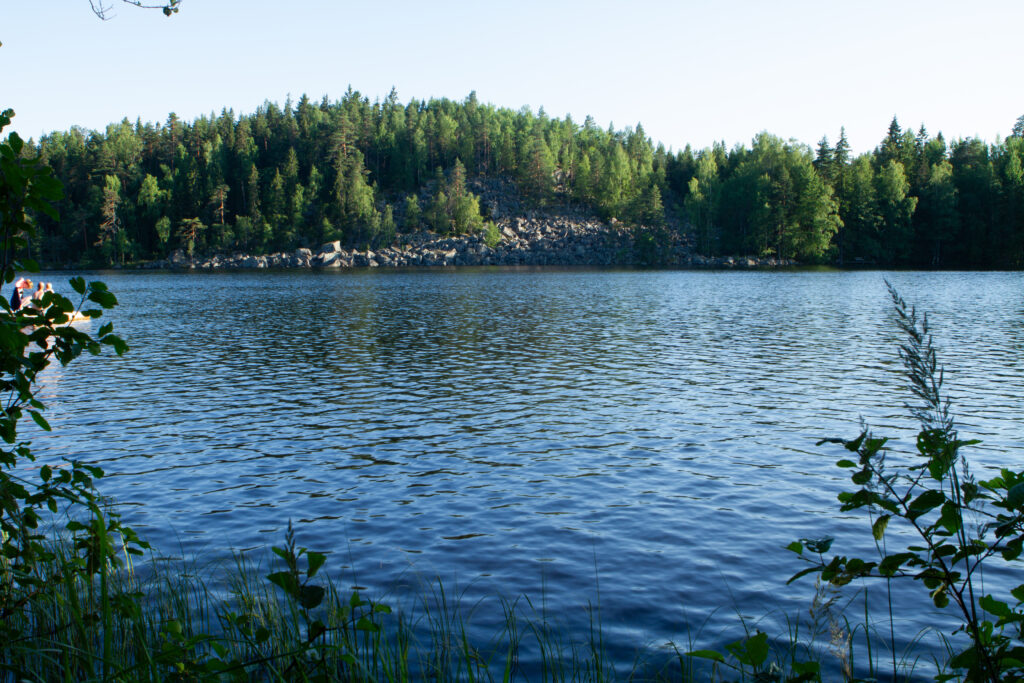 Finnischer See mit leichten Wellen. Das andere Ufer mit Felsen und Bäumen im Hintergrund.